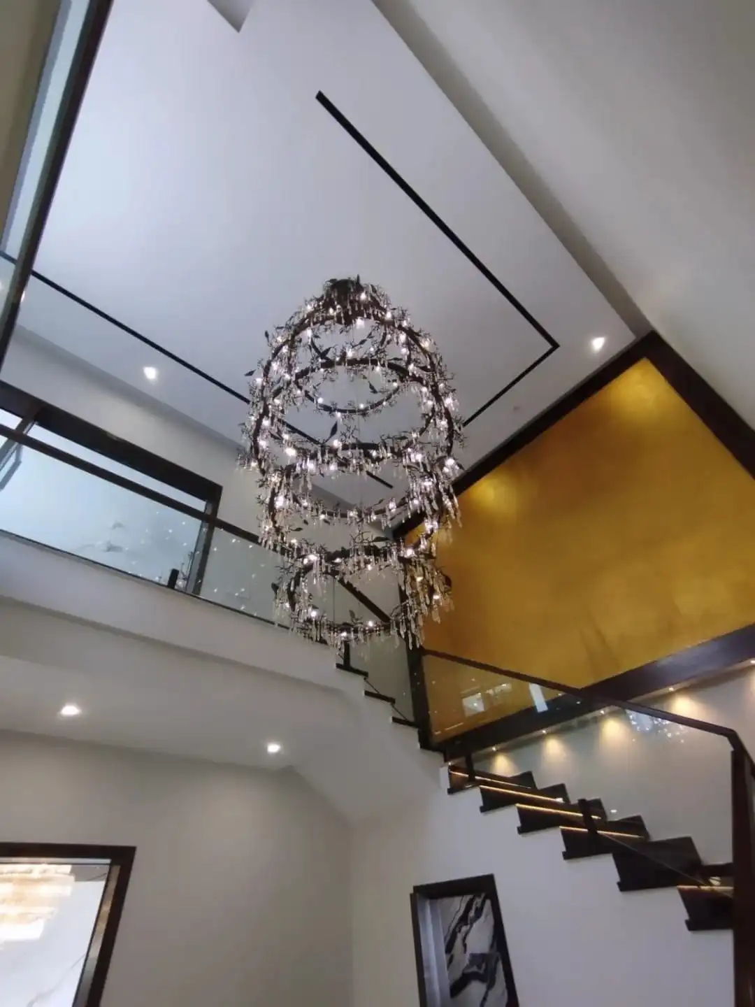 Double height staircase with glass railing sculptural chandelier and gold accent wall in 1 Kanal house Lake City