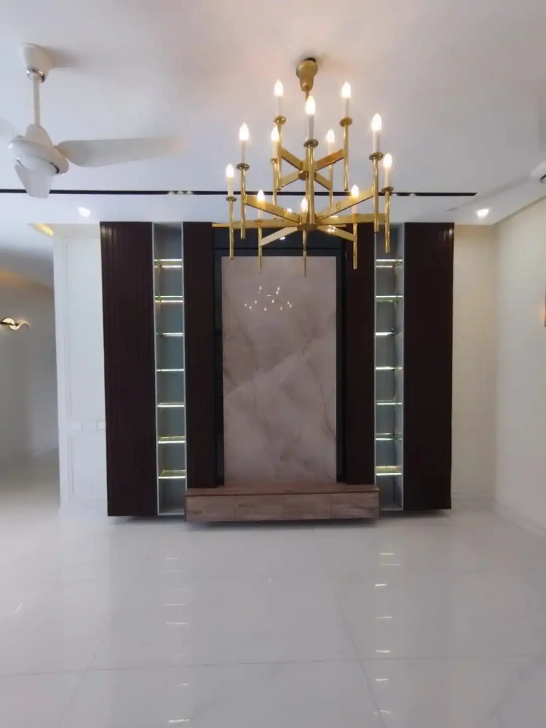 Family TV lounge with dark wood entertainment unit marble panel and gold chandelier in 1 Kanal house Lahore