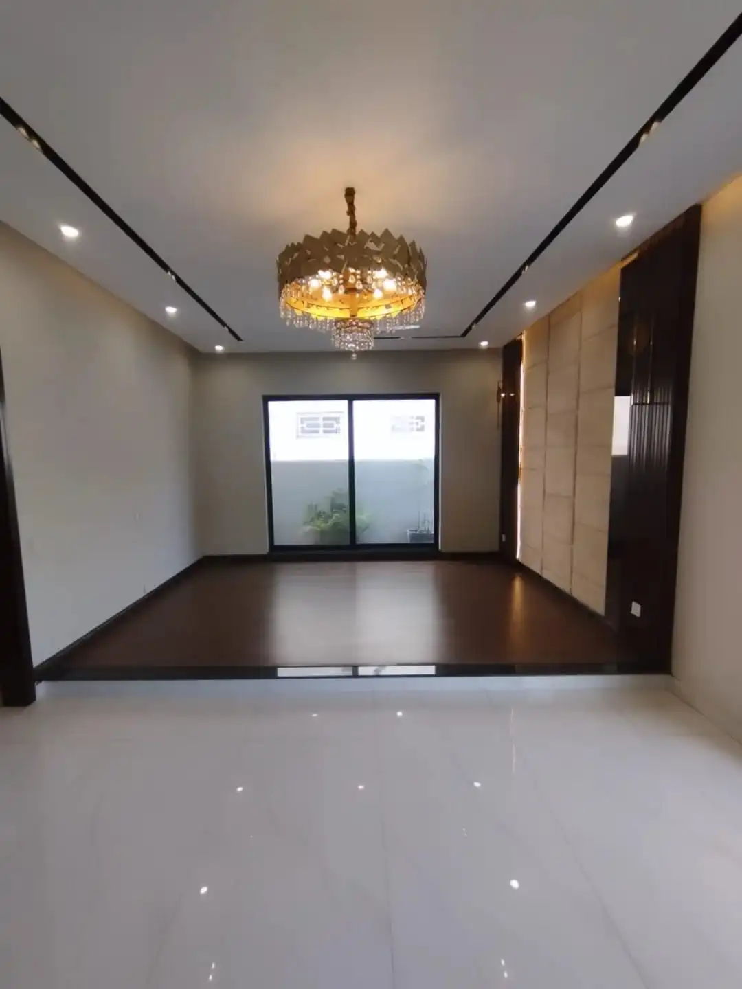 Luxury bedroom with gold chandelier dark wood flooring and padded wall panel in Lake City M3 Lahore