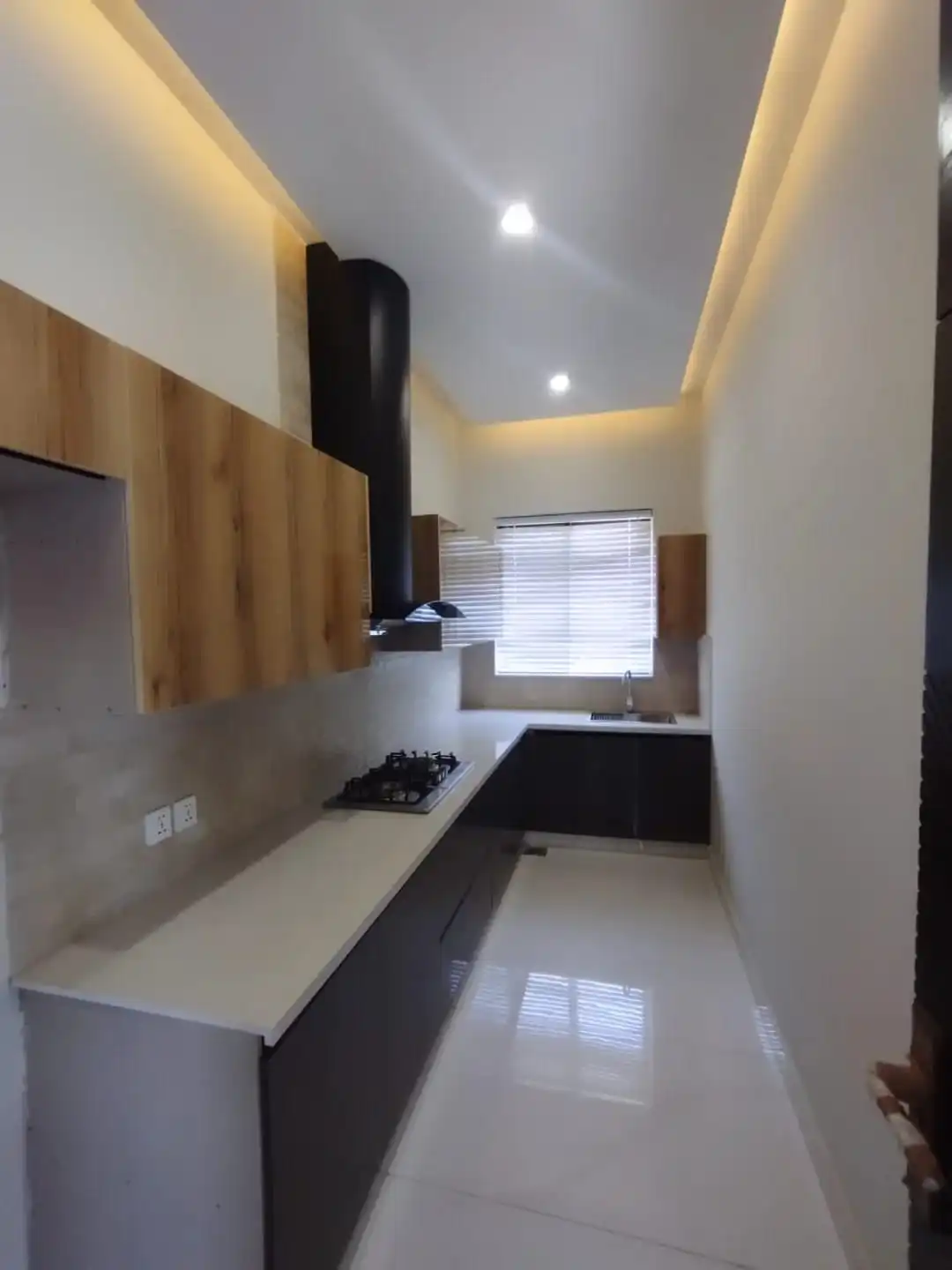 Modern modular kitchen with wooden cabinets and black chimney hood in 1 Kanal house Lake City Lahore