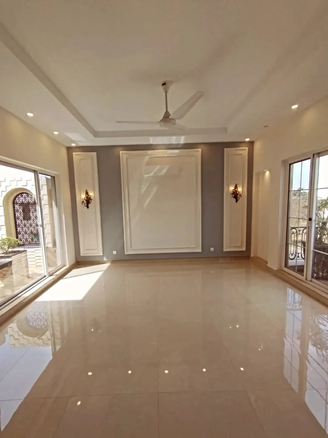 Elegant drawing room with cream marble flooring, grey feature wall and wall sconces in 1 Kanal house Lake City Lahore