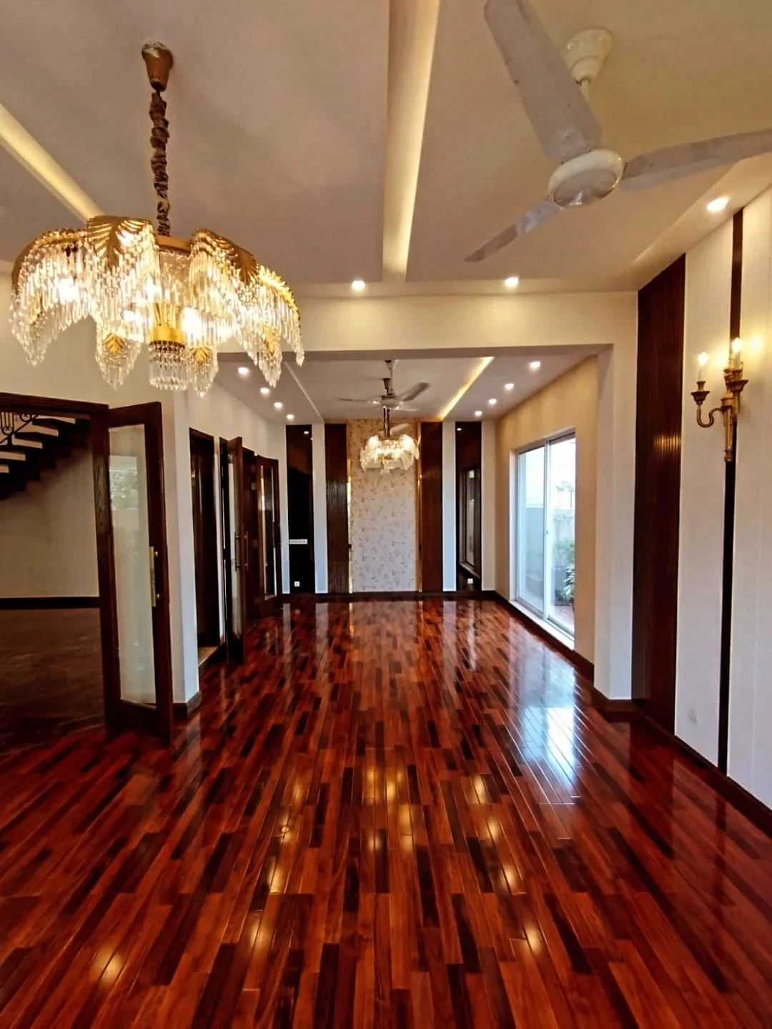 Grand hallway with high gloss wooden flooring, crystal chandeliers and dark wood wall panels in luxury 1 Kanal house Lake City Lahore