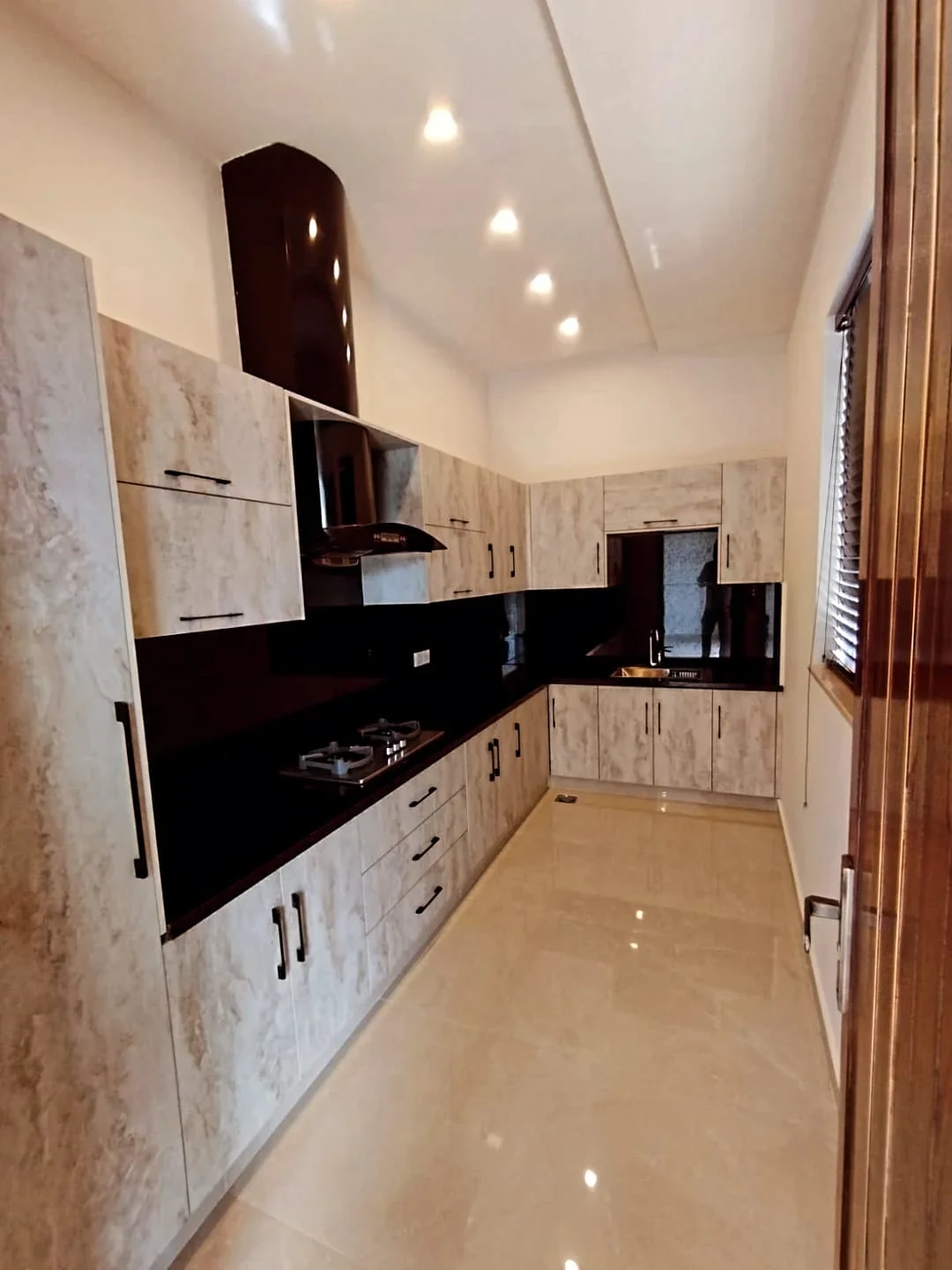 Designer modular kitchen with marble finish cabinets, black granite countertop and chimney hood in 1 Kanal house Lake City Lahore