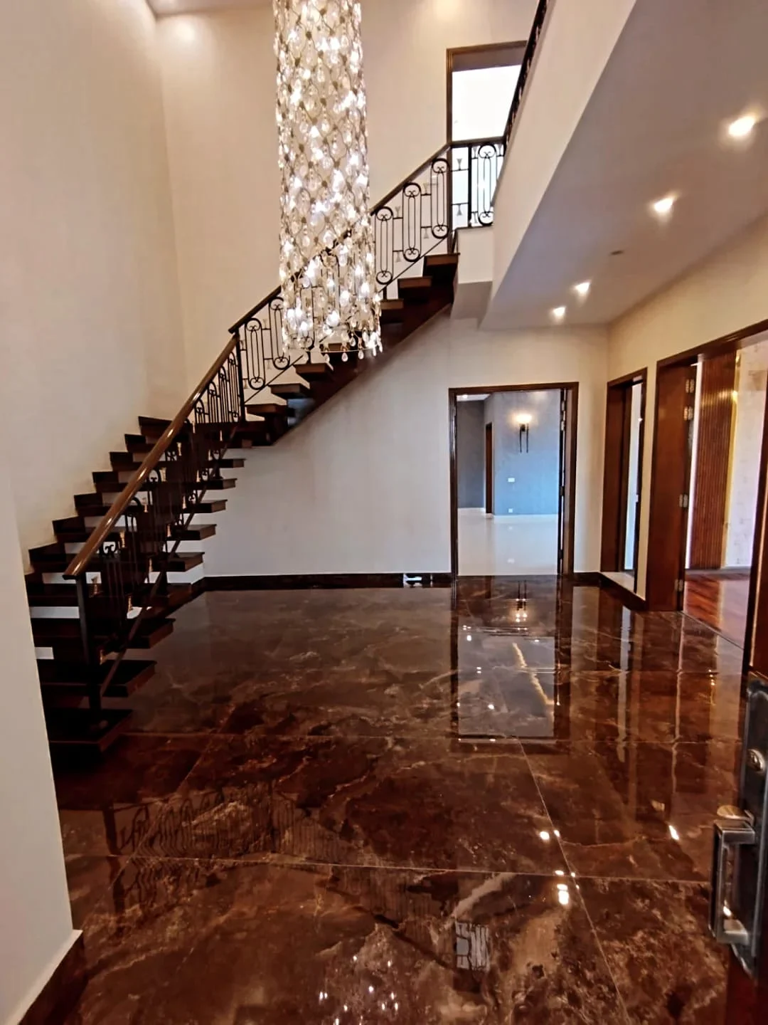 Double height entrance foyer with dark marble flooring, wooden floating staircase and crystal pendant chandelier in 1 Kanal house Lake City
