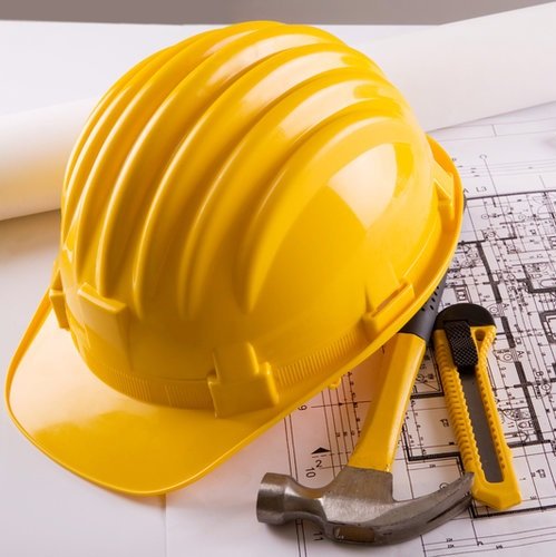 Construction management planning in Lahore, featuring a yellow hard hat, building blueprints, and essential tools used by HMPD project supervisors.