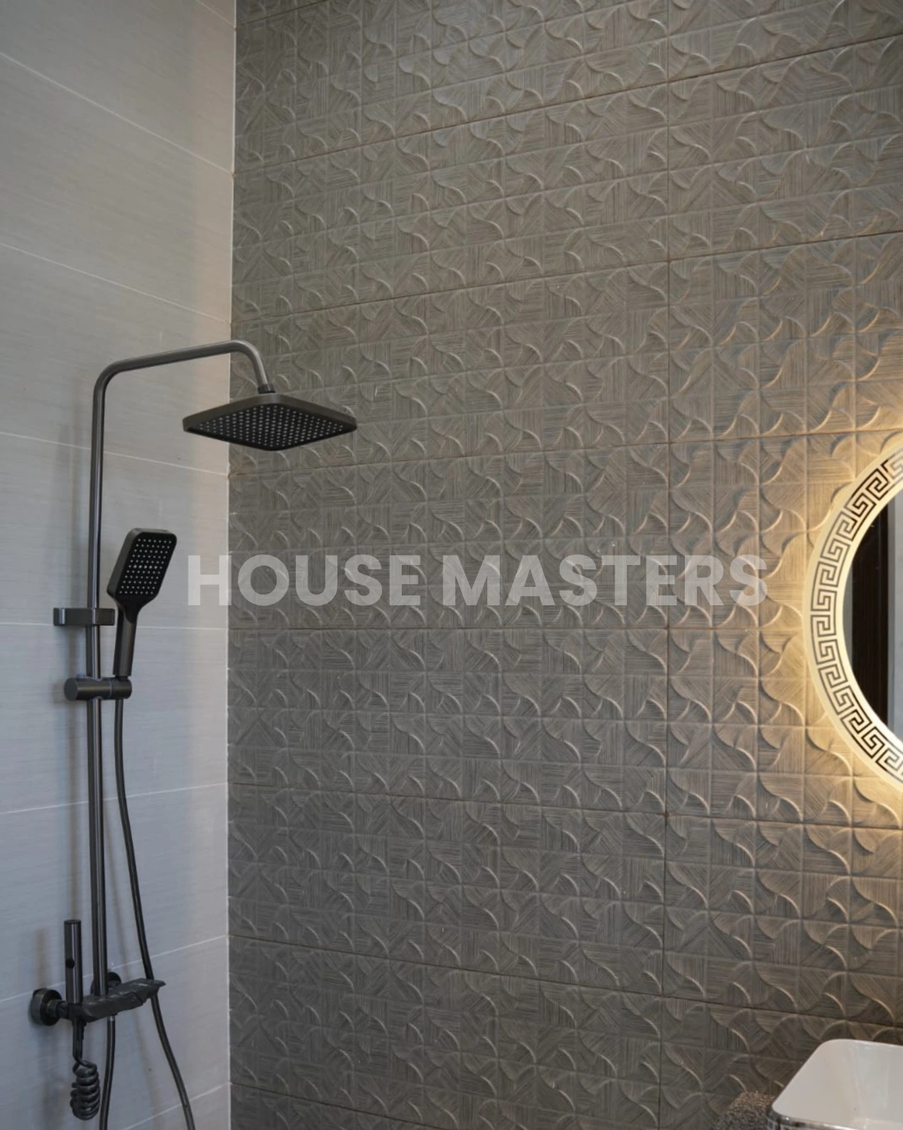 Premium Bathroom Design – 5 Marla House, Bahria Orchard Stylish bathroom with leaf-pattern accent wall, black countertop, and illuminated round mirror in 5 Marla luxury home, Bahria Orchard.