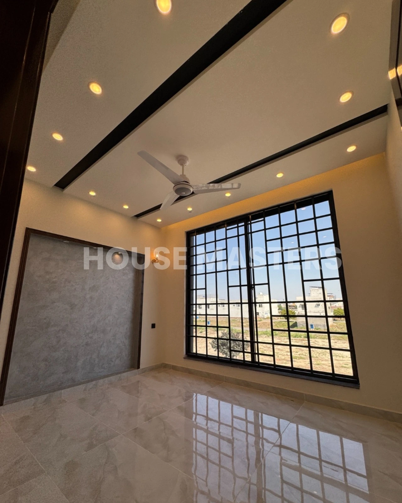 Stylish Bedroom – 5 Marla House in Bahria Orchard, Lahore Modern bedroom with large black-framed windows, ceiling fan, and luxurious flooring in a 5 Marla house, offering scenic views in Bahria Orchard, Lahore.